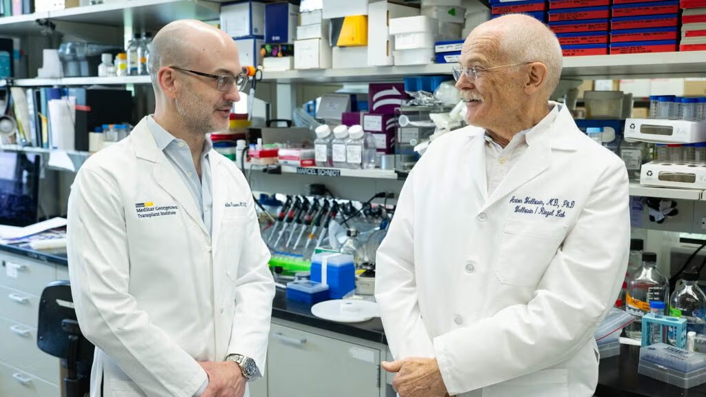 Two men in white coats in a lab in conversation
